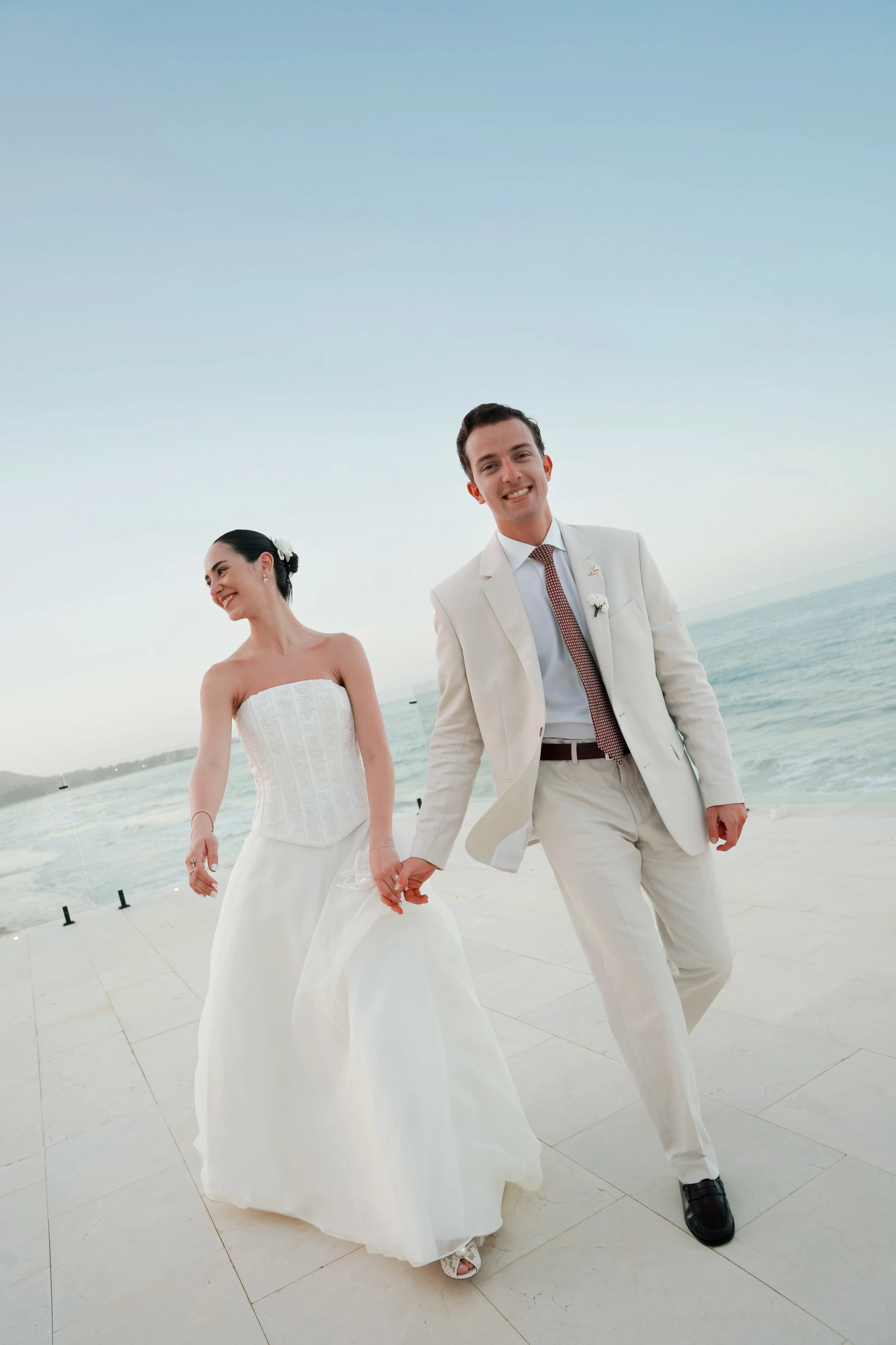 Novios caminando tomados de la mano y sonriendo frente al mar con luz del Caribe, boda editorial en la Isla de Margarita por Andreagsfoto